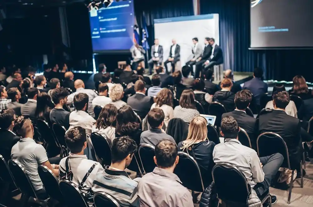 A large crowd gathers in a conference room, engaged in discussions and networking during an event.