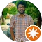 A man wearing a plaid shirt with an orange star prominently displayed on his chest, standing confidently.
